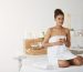 Young beautiful african girl in towel smiling holding glass with tea sitting in spa salon.
