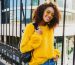 Outdoor bright portrait of happy African girl with back pack  and standing on urban background. Wearing yellow sweater and sunglasses. Pretty student enjoying sunny spring day.